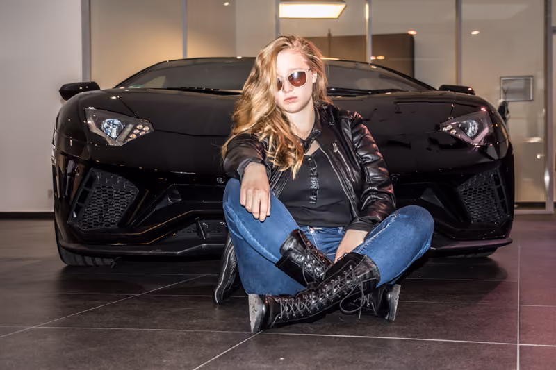 Frau mit Sonnenbrille sitzt vor einem schwarzen Sportwagen